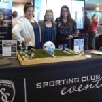 Three people at a publicity table at an event promoting Sporting club events