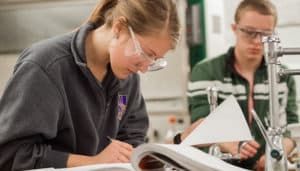 Student with lab googles makes notes in a book